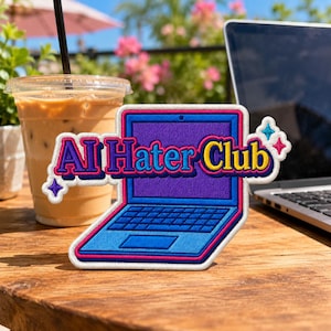 May include: A rectangular embroidered patch shaped like an open laptop with a purple screen and blue keyboard. The text AI Hater Club is stitched in yellow and purple across the center. Two small four-pointed stars in blue and pink accent the design.