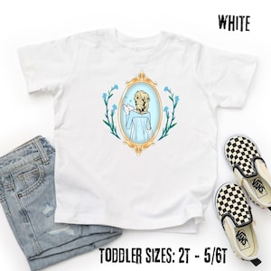 May include: White toddler t-shirt featuring a cartoon illustration of a character in a gold-framed mirror, surrounded by blue flowers. The text "WHITE" is at the top, and "TODDLER SIZES: 2T - 5/6T" is at the bottom. A pair of black and white checkered slip-on shoes and blue jeans are also in the image.