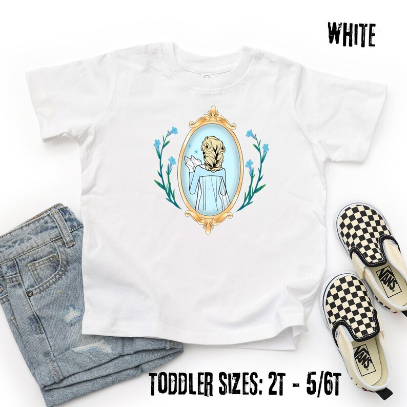 May include: White toddler t-shirt featuring a cartoon illustration of a character in a gold-framed mirror, surrounded by blue flowers. The text "WHITE" is at the top, and "TODDLER SIZES: 2T - 5/6T" is at the bottom. A pair of black and white checkered slip-on shoes and blue jeans are also in the image.