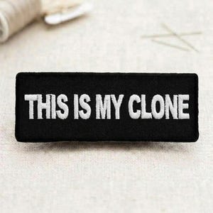 May include: Black rectangular patch with white embroidered text that reads "THIS IS MY CLONE". The patch is likely made of fabric and has a stitched border. The background is a light, neutral color.