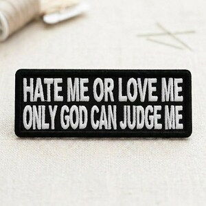 May include: Black rectangular patch with white embroidered text that reads "HATE ME OR LOVE ME ONLY GOD CAN JUDGE ME". The patch is likely for clothing or accessories.