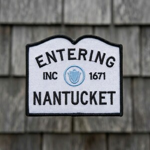 May include: A white patch with a black border and the words "ENTERING NANTUCKET" in black. The patch also includes "INC 1671" and a light blue emblem.