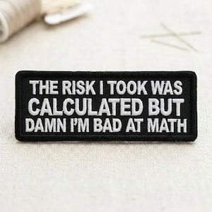 May include: A black rectangular patch with white embroidered text that reads: "THE RISK I TOOK WAS CALCULATED BUT DAMN I'M BAD AT MATH". The patch is likely for clothing or accessories.