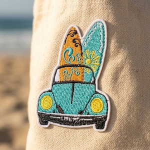 May include: An embroidered patch featuring a teal car with yellow headlights and a black bumper. Two surfboards are strapped to the roof: one orange with black swirls and one teal with a yellow sun design. The patch is attached to beige fabric.