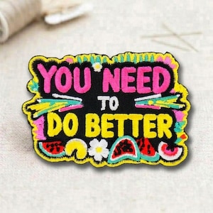 May include: Embroidered patch with the text "YOU NEED TO DO BETTER" in pink and yellow. The patch has a black background with colorful accents, including watermelon slices and flowers. The patch is outlined in yellow.