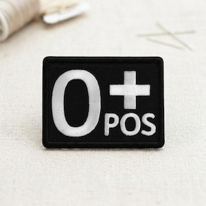 May include: A black rectangular patch with white text reading "0+ POS". The "0" is large, the "+" is a cross, and "POS" is below the cross. The patch is likely an embroidered or printed design.