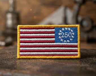 May include: Embroidered patch featuring the American flag design with red and white stripes, a blue corner with white stars, and the number "250". The patch has a yellow border.