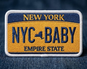 May include: Embroidered patch in the shape of a New York license plate. The patch features the text "NEW YORK" above "NYC BABY" with a silhouette of the state and "EMPIRE STATE" below, in navy blue and gold.