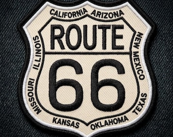 May include: A Route 66 patch in a shield shape, featuring the words "ROUTE 66" and the number "66" in bold black lettering. The patch includes the names of states like California, Arizona, and Texas, with a cream-colored background and black border.