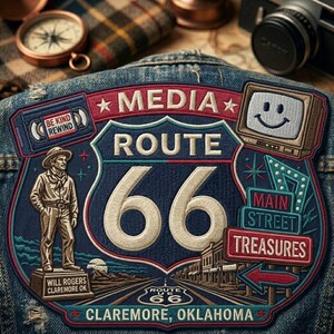 May include: A denim jacket with a large embroidered patch featuring a Route 66 design. The patch includes the words "MEDIA ROUTE 66", a vintage television with a smiley face, and the text "MAIN STREET TREASURES". Additional text includes "BE KIND REWIND" and "CLAREMORE, OKLAHOMA".