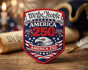 May include: A patriotic patch with a shield shape, featuring the text "We the People" and "America 250". The design includes an eagle, stars, and fireworks in red, white, and blue. The patch is likely for apparel or collectibles.