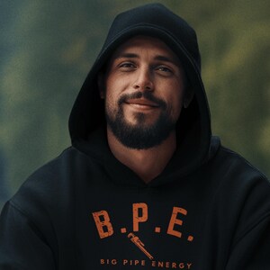 Puede incluir: Una sudadera con capucha negra con el texto naranja "B.P.E." y un gráfico de llave inglesa. Debajo, las palabras "BIG PIPE ENERGY" están impresas en naranja. La persona de la imagen lleva la sudadera con capucha.