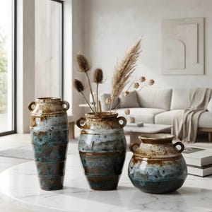 Könnte beinhalten: Set aus drei Keramikbechern mit gesprenkelter, matter Oberfläche. Jeder Becher hat eine andere Farbe: hellblau, creme und grau. Die Becher haben ein schlichtes, modernes Design und einen bequemen Griff.