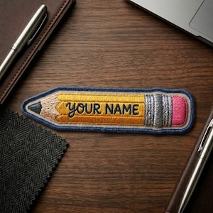 May include: An embroidered patch shaped like a yellow pencil with a dark gray tip, a silver ferrule, and a pink eraser. The center of the pencil features the text "YOUR NAME" stitched in dark blue thread, outlined by a dark blue border.