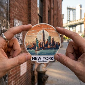 May include: A circular embroidered patch featuring a detailed New York City skyline with the Statue of Liberty in the foreground against a large sun. The text NEW YORK United States is printed in black on a white tab at the bottom of the patch.