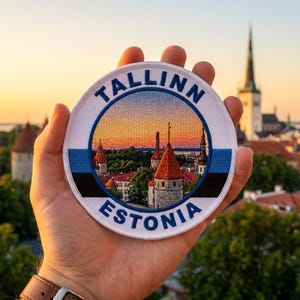 May include: A round patch featuring a scenic view of Tallinn, Estonia, with the text "TALLINN ESTONIA" in a circular design. The patch incorporates the colors of the Estonian flag: blue, black, and white. The background shows a sunset over the city.