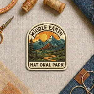 May include: An embroidered patch with a rounded top edge featuring a landscape of mountains, a winding river, and a sun. The text reads MIDDLE EARTH at the top and NATIONAL PARK at the bottom in dark brown lettering on a cream-colored background.