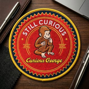 May include: Embroidered patch featuring Curious George, the curious monkey, in a seated pose. The patch is circular with a red background and the words "STILL CURIOUS" and "Curious George" in white. The patch also includes the year "1941".