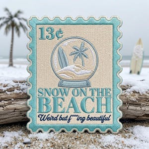 May include: A rectangular embroidered patch shaped like a postage stamp with a light blue border. It features a snow globe graphic containing a surfboard, palm tree, and sand. Text reads 13 cents, SNOW ON THE BEACH, and Weird but f***ing beautiful.