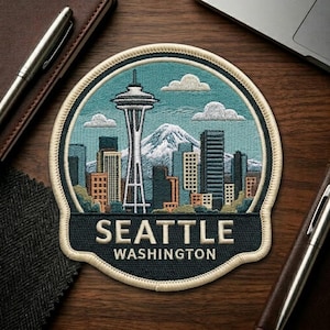 May include: Embroidered patch featuring the Seattle skyline, including the Space Needle, mountains, and city buildings. The patch is in a circular shape with the words "SEATTLE WASHINGTON" at the bottom. The patch has a blue, green, white, and tan color scheme.