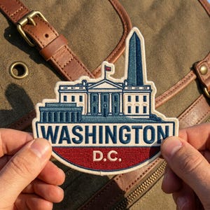 May include: An embroidered patch featuring the White House and the Washington Monument in blue and white thread. The text WASHINGTON D.C. is stitched in blue and white on a red background. The patch has a cream-colored border and backing.