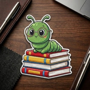 May include: A green caterpillar wearing glasses sits atop a stack of books. The books have red, yellow, and blue spines. The caterpillar is smiling. The patch is on a wooden surface.