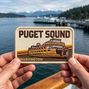 May include: A rectangular patch with the words "PUGET SOUND" in brown letters above a ferry illustration. The ferry is brown and yellow, with the word "WASHINGTON" below. The background shows a ferry on the water, mountains, and trees.