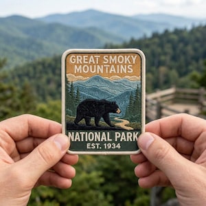May include: A rectangular embroidered patch featuring a black bear walking through a forest with blue mountains in the background. The text reads GREAT SMOKY MOUNTAINS NATIONAL PARK EST. 1934 in white and tan lettering against a tan and green background.