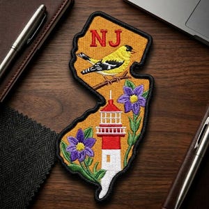 May include: Embroidered patch in the shape of New Jersey, featuring a yellow bird, purple flowers, and a red and white lighthouse. The letters "NJ" are in red at the top. The patch has a black border and is on a tan background.
