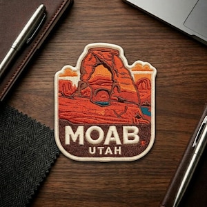 May include: Embroidered patch featuring a scenic view of Moab, Utah, with a prominent arch and desert landscape in shades of orange, red, and brown. The patch includes the text "MOAB UTAH" in white letters.