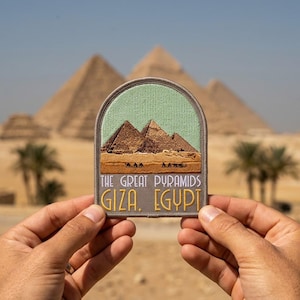 May include: A semi-circular embroidered patch featuring a light green sky above brown pyramids and a desert landscape with small camel silhouettes. The text reads THE GREAT PYRAMIDS GIZA, EGYPT in white and yellow thread on a grey background.