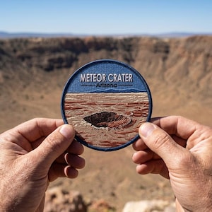 May include: A round embroidered patch featuring the Meteor Crater in Arizona. The patch has a blue border with the words "METEOR CRATER Arizona" in white. The center depicts the crater in shades of brown and tan.