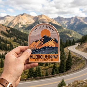 May include: A patch featuring a mountain landscape with the text "San Juan Skyway" and "Million Dollar Highway Colorado." The design includes a road, mountains, and a setting sun, with a color palette of orange, brown, and green.