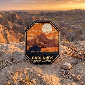 May include: An octagonal embroidered patch featuring a landscape of the Badlands National Park. The design includes a black bison, brown mountains, a white sun, and orange clouds against a sunset sky. The text 1978, BADLANDS, and NATIONAL PARK is visible.