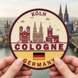 May include: A round patch featuring the Cologne skyline with the words "KÖLN" and "COLOGNE" in burgundy. The German flag is at the bottom, with "GERMANY" below it. The patch is held by two hands.