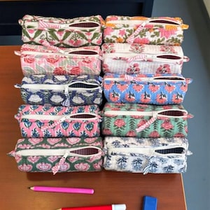 May include: Ten rectangular quilted pencil cases arranged in two columns, each featuring a white zip and distinct floral block-print patterns in various colours including pink, green, blue, and white, accompanied by two pens and a blue eraser.