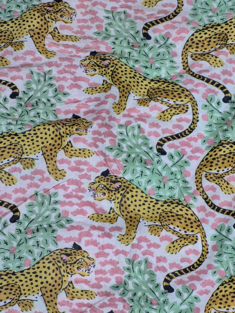 May include: A repeating pattern of yellow leopards with black spots and tails on a white background. The leopards are interspersed with pink floral and green leafy elements. The design has a vintage, jungle-inspired aesthetic.