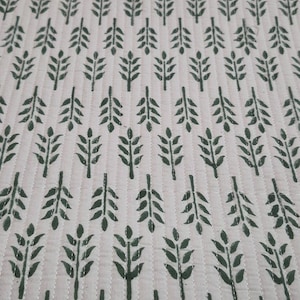 May include: Cream-colored quilted fabric with a repeating pattern of dark green leaf sprigs. The leaves are arranged in vertical rows, with white stitching creating a grid-like texture. The fabric has a soft, inviting appearance.