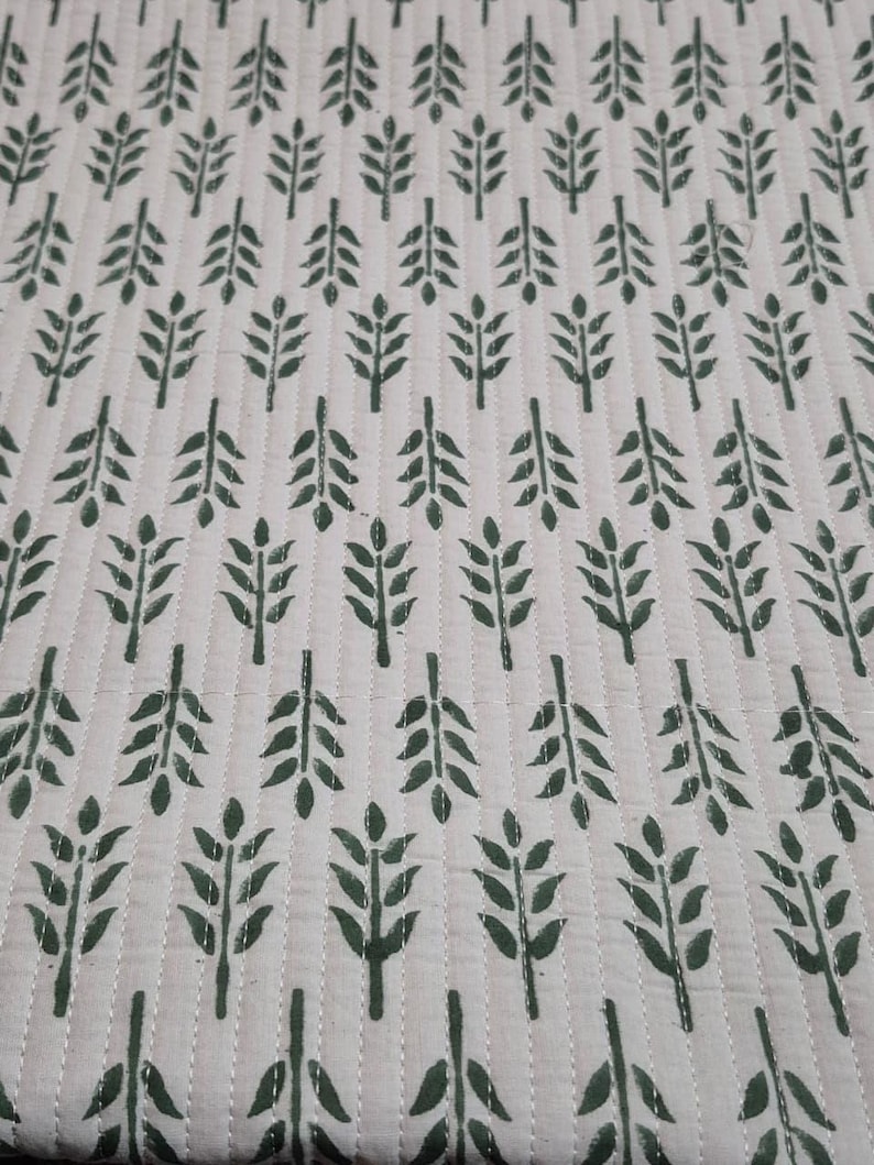 May include: Cream-colored quilted fabric with a repeating pattern of dark green leaf sprigs. The leaves are arranged in vertical rows, with white stitching creating a grid-like texture. The fabric has a soft, inviting appearance.