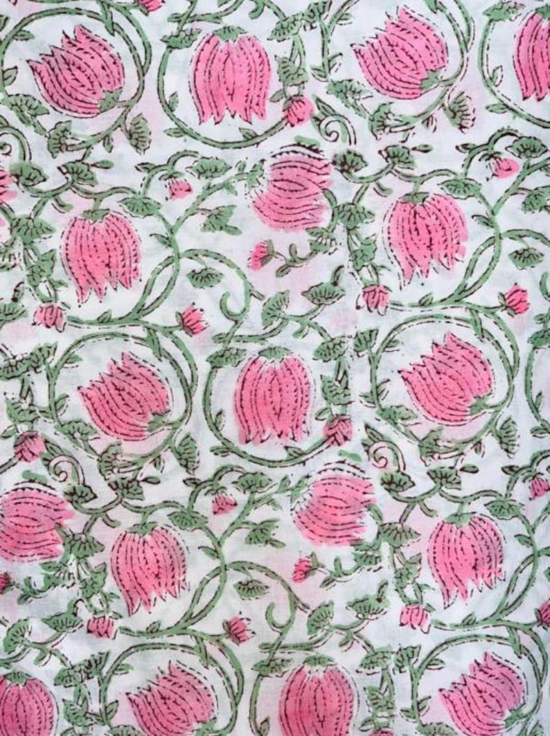 May include: White fabric with a repeating pattern of pink flowers and green vines. The flowers are stylized with detailed petals, and the vines have small leaves. The design is printed on a white background, creating a floral textile.