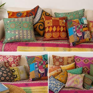 May include: A collection of square and rectangular throw pillows featuring diverse patchwork designs, intricate kantha stitching, and vibrant color palettes including teal, red, yellow, and blue, arranged on a pink and yellow patterned fabric surface.
