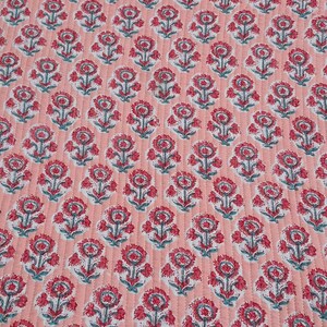 May include: A quilted fabric with a repeating floral pattern. The flowers are red with white and teal accents, set against a light coral background. The fabric has a stitched, textured appearance.