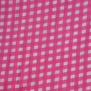 May include: A close-up shot of a pink and white checkered fabric. The pattern consists of a grid of white squares against a bright pink background. The fabric appears to be slightly wrinkled, adding texture to the design.