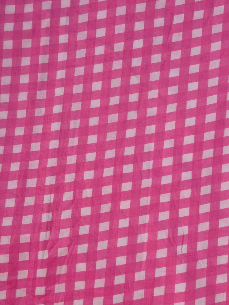 May include: A close-up shot of a pink and white checkered fabric. The pattern consists of a grid of white squares against a bright pink background. The fabric appears to be slightly wrinkled, adding texture to the design.