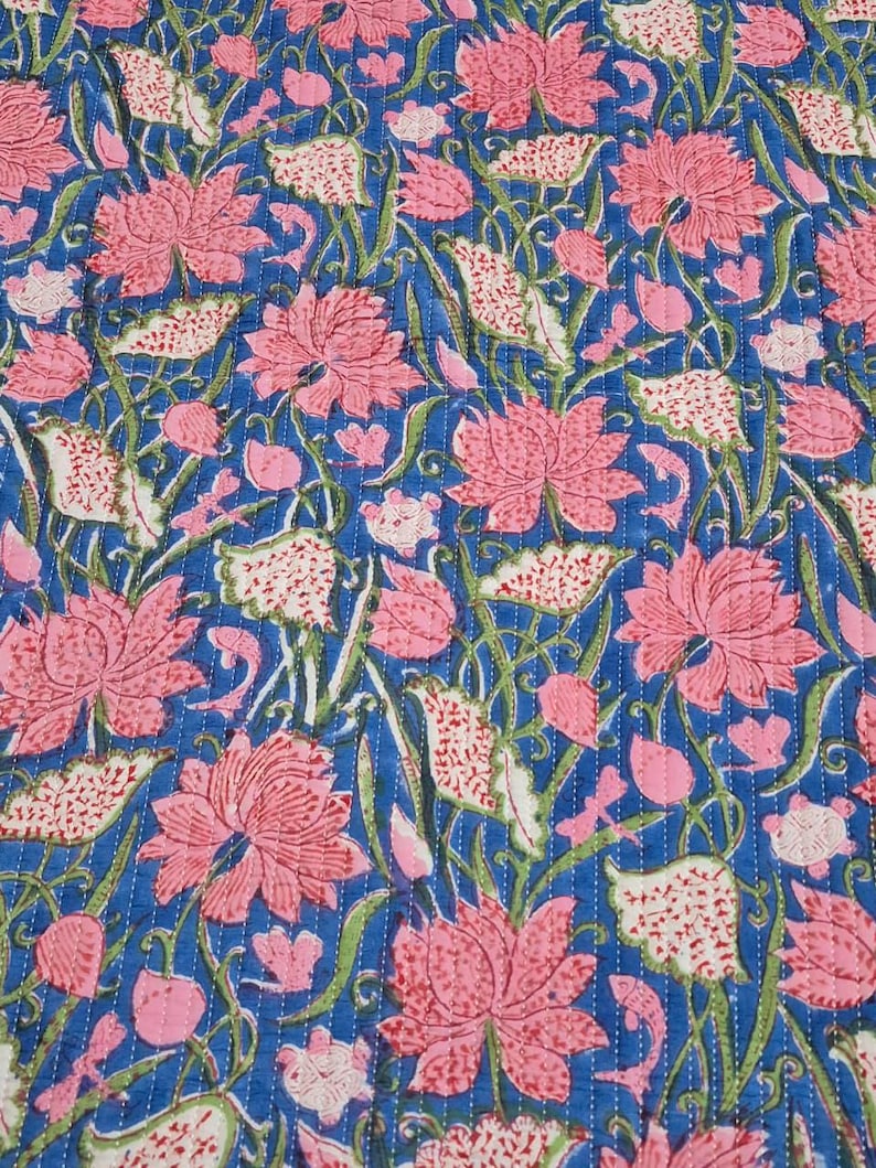 May include: A blue floral quilt with a repeating pattern of pink lotus flowers and white leaves. The quilt is stitched with white thread, creating a textured effect. The design is a mix of floral and botanical elements.