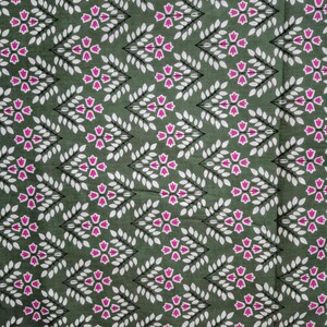 May include: A close-up of a fabric with a repeating pattern of white leaves and pink floral shapes on a dark green background. The design is arranged in diagonal rows, creating a textured appearance.