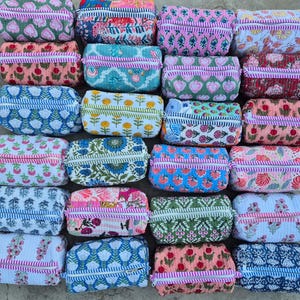 May include: A collection of twenty-four rectangular quilted pouches arranged in a grid. Each pouch features a unique floral or geometric block-print pattern in various colors, including pink, blue, green, and red, with a zippered closure.