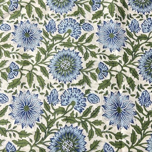 May include: Floral fabric with a repeating pattern of large blue flowers and green leaves on a cream background. The flowers have detailed petals and are surrounded by smaller buds and foliage. The design is symmetrical and creates a visually appealing textile.