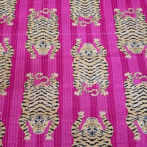 May include: A vibrant pink textile featuring a repeating pattern of stylized tigers. The tigers are depicted in tan and black stripes, with their paws raised. The background has vertical stripes, and the fabric appears to be quilted.