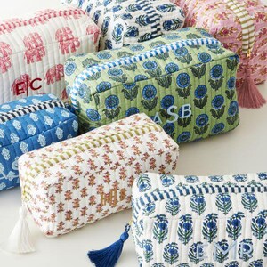 May include: A collection of rectangular quilted fabric pouches featuring various block-print patterns in blue, green, pink, and red. Each pouch includes a zippered closure with a decorative tassel and embroidered monogram initials on the front.